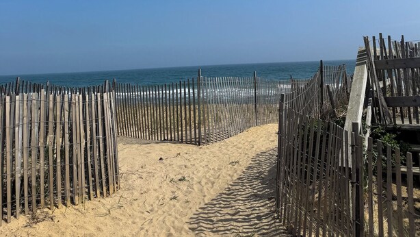 Un sentier de sable bordé d’une clôture en bois qui mène à l’océan.