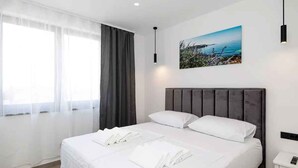 A modern hotel room with a large bed, a painting of a coastal scene, and a small bedside table with a lamp. - Holiday home with swimming pool fully equipped (Dramalj)