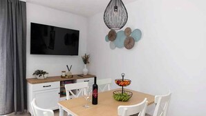 A dining area with a wooden table, white chairs, a TV mounted on the wall, and decorative wall art. - Holiday home with swimming pool fully equipped (Dramalj)