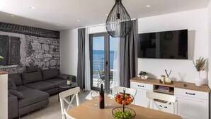 A modern living room with a sofa, dining table, and a TV mounted on the wall. - Holiday home with swimming pool fully equipped (Dramalj)