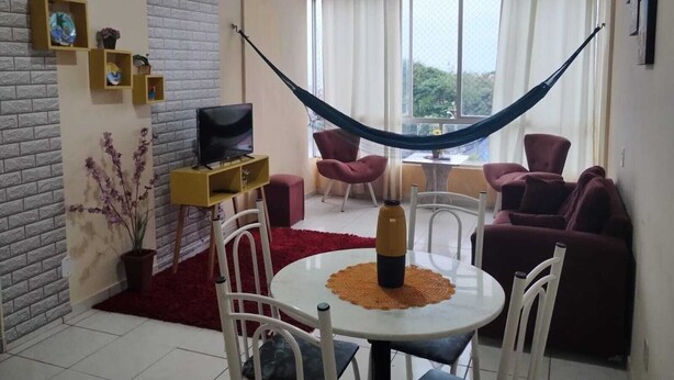 A living room with a TV, red chairs, a hammock, and a view of greenery outside. - Apartment for the season in Praia do Futuro (Antonio Diogo Fortaleza)