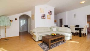 Ein modernes Wohnzimmer mit einem weißen Sofa, einem Couchtisch mit Obst und einem Essbereich mit Stühlen und einem Tisch.