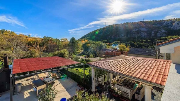 Ein Wohngebiet mit einem Gebäude mit rotem Dach, einer überdachten Terrasse und Blick auf eine hügelige Landschaft.