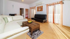 Ein Wohnzimmer mit einem weißen Sofa, einem schwarzen Sofa, einem Couchtisch aus Holz mit Früchten und einem grauen Teppich.