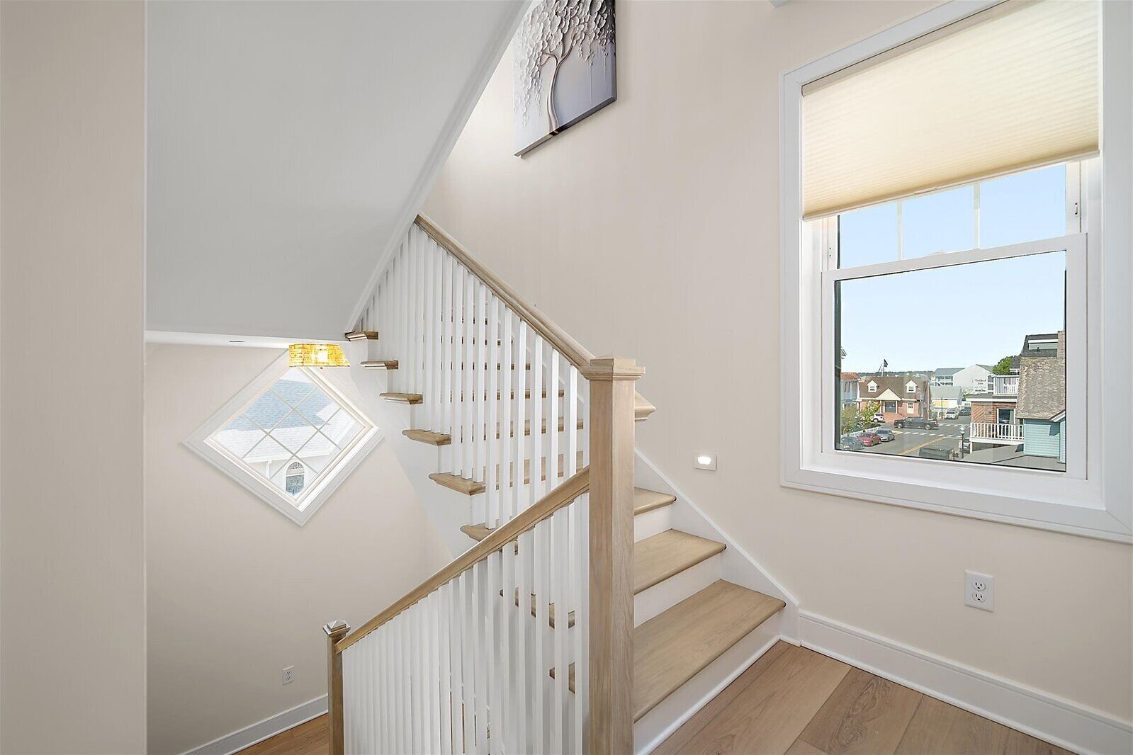 A staircase with white railings and wooden steps leading to a landing with a window offering a view of the street.