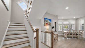 A spacious interior with a wooden staircase, a dining area with a table and chairs, and a view through the open door.