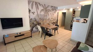 A compact living space with a dining area, a TV mounted on the wall, and a kitchen area.