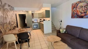 A compact living space with a dining area, a sofa, a small coffee table, and a kitchen in the background.