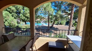 A covered outdoor seating area with a table and chairs, overlooking a pool and trees.