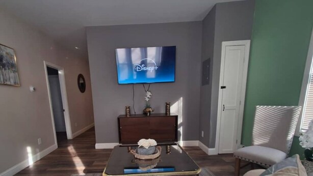 Un salon avec un téléviseur à écran plat fixé au mur, une table basse en bois foncé, un fauteuil blanc et un mur d’accent vert.