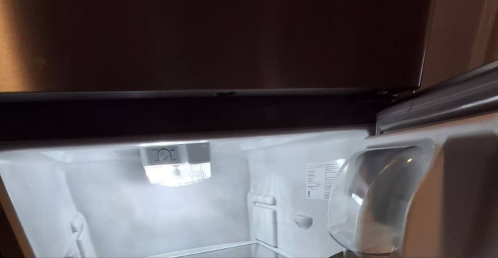 Insidan av ett kylskåp med en transparent dörr, en kontrollpanel och en etikett på dörren.