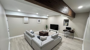 A modern living room with a sectional sofa, a flat-screen TV, a desk, and a potted plant.