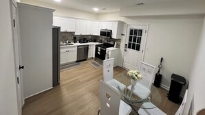 A modern kitchen with white cabinets, stainless steel appliances, and a dining area with a glass table and chairs.