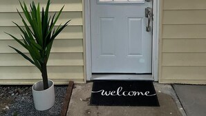 A white door with a glass panel, a welcome mat, and a potted plant beside it.