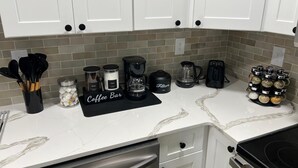 A kitchen with white cabinets, a coffee bar, a coffee maker, a blender, a toaster, and a spice rack.