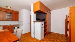 A compact kitchen with wooden cabinets, a white refrigerator, and a dining table with chairs. - Studio with air conditioning and washing machine (Crikvenica)