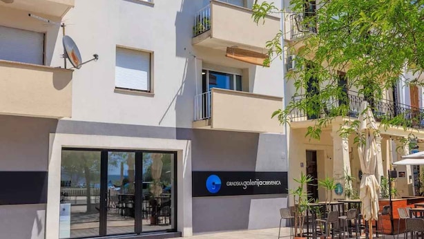 A building with a sign reading "Gradska Galenija Krivićnica" and outdoor seating with umbrellas. - Holiday apartment on the promenade (Crikvenica)