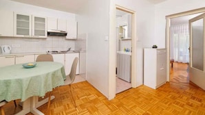 A compact kitchen with white cabinets, a dining table with a green tablecloth, and a wooden floor. - Holiday apartment on the promenade (Crikvenica)