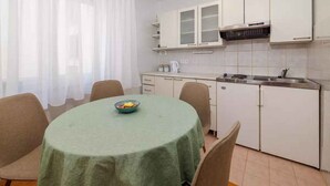 A small, modern kitchen with white cabinets, a stainless steel sink, and a round table with a green tablecloth. - Holiday apartment on the promenade (Crikvenica)