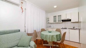 A compact living space with a sofa, a dining table with chairs, a kitchenette, and a window with curtains. - Holiday apartment on the promenade (Crikvenica)