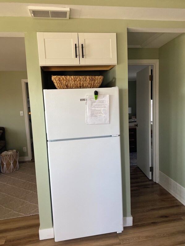 A kitchen with a white refrigerator, a woven basket on top, and a cabinet above.