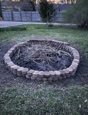 A circular garden bed with a brick border, surrounded by grass and a wooden fence.