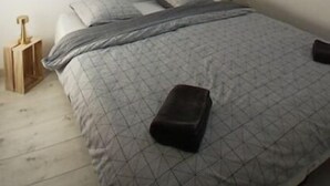 Un dormitorio con techo inclinado, un tragaluz, una cama con colcha estampada y una mesita de noche con lámpara.