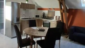 Una cocina compacta con electrodomésticos modernos, un comedor con una mesa redonda y sillas, y vigas de madera a la vista en el techo.