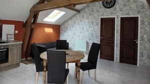Un comedor con una mesa redonda de madera y sillas negras, una cocina con horno empotrado y un techo abovedado con vigas de madera a la vista.