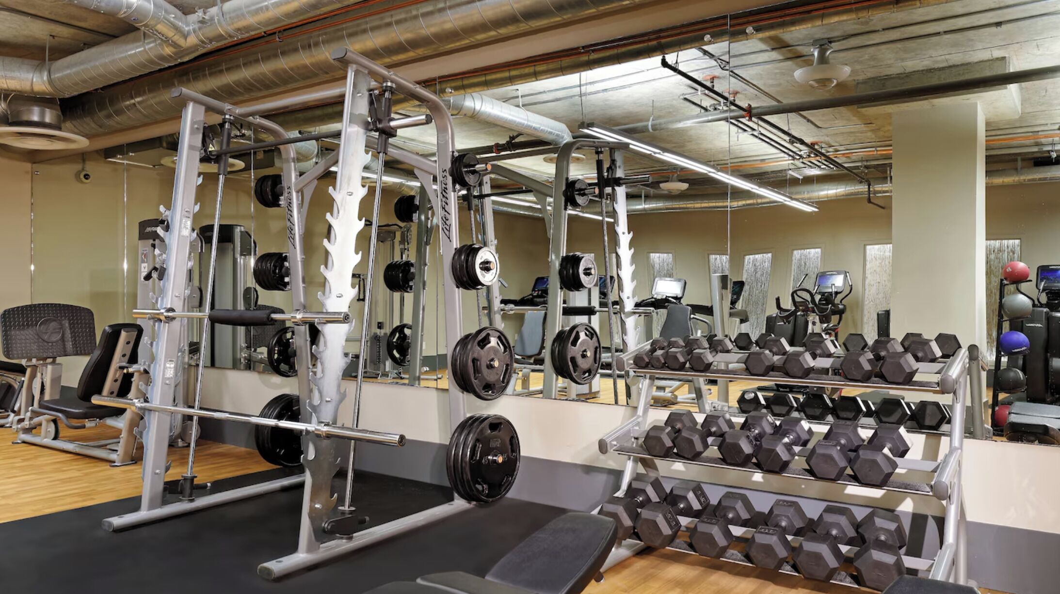 Une salle de sport équipée de matériel de musculation, de miroirs et de ballons d’exercice.