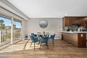 Une cuisine moderne avec des meubles en bois, une table de salle à manger ronde entourée de chaises bleues et une grande fenêtre donnant sur un balcon.