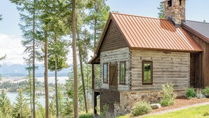 Une cabane en rondins avec des fondations en pierre, un toit en métal et une vue sur un lac et des montagnes.