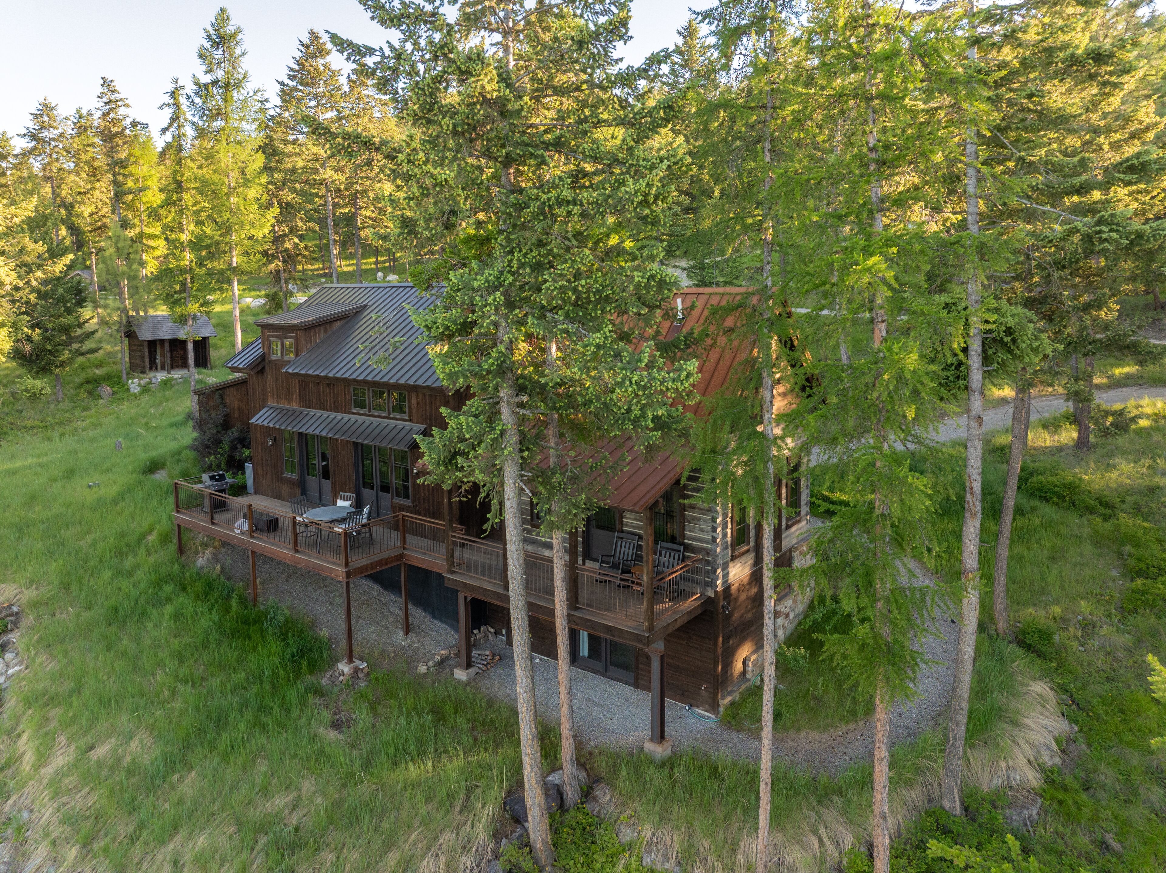 Une cabane dotée d’une terrasse, entourée d’arbres et bordée d’une pelouse.