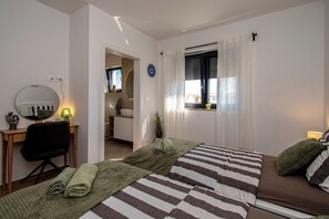 Quarto com cama, escrivaninha, cadeira, espelho e janela com cortinas.