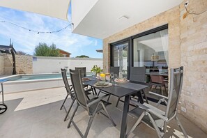 Een terras buiten met een zwembad, een eettafel met stoelen, en uitzicht op de keuken door een glazen deur.
