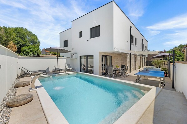 Um edifício moderno de dois andares com piscina, área de estar ao ar livre e mesa de pingue-pongue.