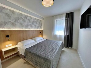 A modern hotel room with a large bed, a bedside table, a wall-mounted lamp, and a window with curtains.