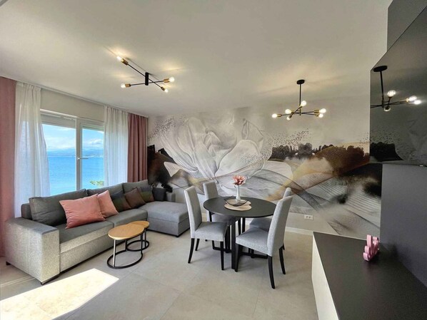 A modern living room with a grey sofa, a dining table with chairs, and a large abstract mural on the wall.