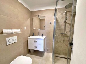 A modern bathroom with a glass-enclosed shower, a white sink, and a large mirror.