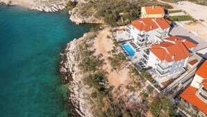 Une propriété située sur la côte, comprenant plusieurs bâtiments, une piscine et une plage rocheuse.