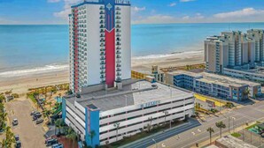 A high-rise hotel with a central tower and a parking garage, located near a beach. - Cozy 1-bedroom condo - direct ocean view in Myrtle Beach with fitness room (Myrtle Beach)