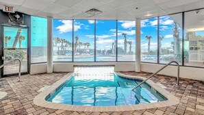 An indoor swimming pool with clear views of palm trees and a clear sky through large windows. - Cozy 1-bedroom condo - direct ocean view in Myrtle Beach with fitness room (Myrtle Beach)