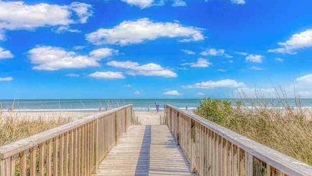 A wooden boardwalk leading to a beach with a clear blue sky and scattered clouds. - Cozy 1-bedroom condo - direct ocean view in Myrtle Beach with fitness room (Myrtle Beach)