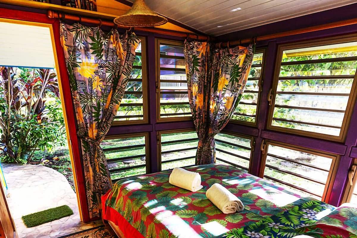 Ein Schlafzimmer mit Bett, Vorhängen und Blick auf Grünfläche.