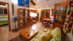 Una sala de estar acogedora con un sofá, una mesa de centro y una estantería. Se observa una mesa de comedor con sillas y una zona de cocina con refrigerador y estufa.