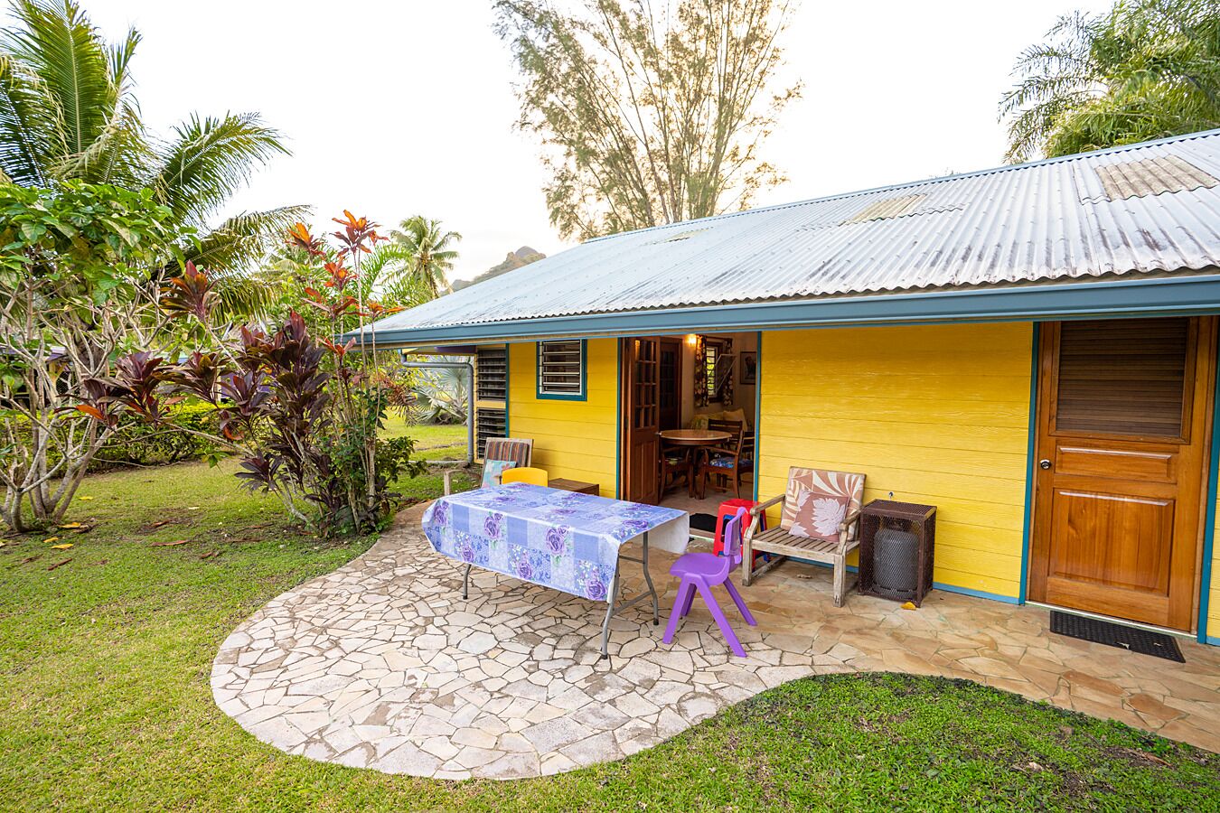 Une maison dotée d’un patio comprenant une table et des chaises, entouré d’un chemin de pierre et d’une végétation luxuriante.