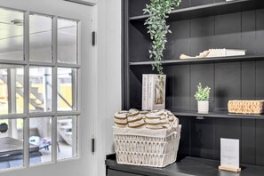 Una habitación con una puerta blanca, una cesta de toallas a rayas, una planta en maceta y un estante con libros y un letrero.