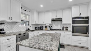 Una cocina moderna con armarios blancos, encimeras de granito y electrodomésticos de acero inoxidable.