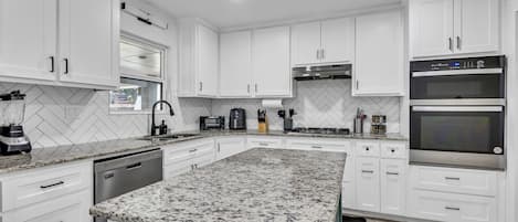 A modern kitchen with white cabinets, granite countertops, and stainless steel appliances.