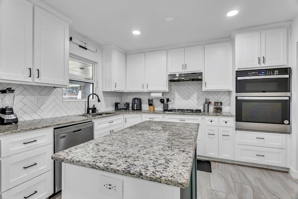 A modern kitchen with white cabinets, granite countertops, and stainless steel appliances.